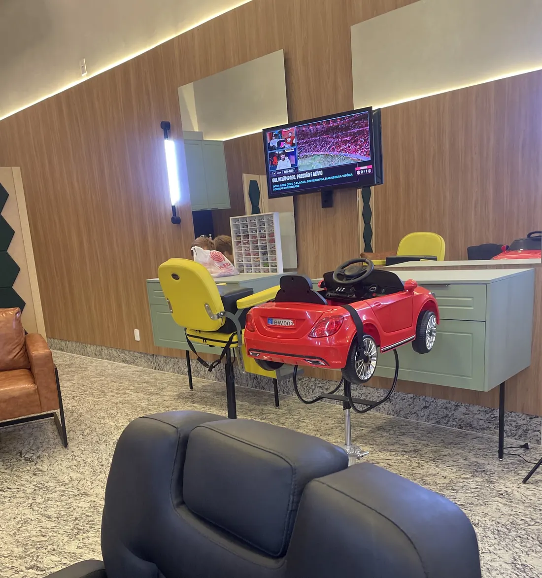 Cadeira de barbeiro preta em primeiro plano e cadeiras em forma de carrinho vermelho e amarelo ao fundo